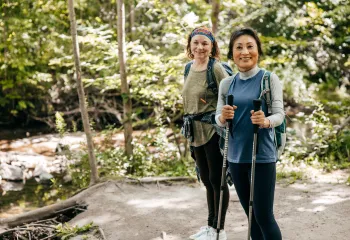 Two women outdoors walking together. One of the women is holding walking poles.