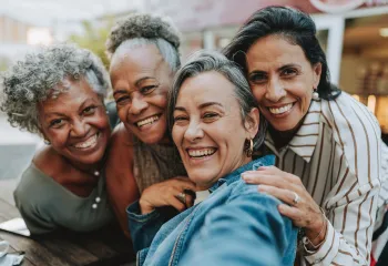 A group of women taking a selfie outdoors. They are smiling at the camera.
