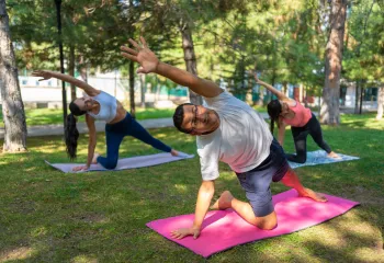 A man in a group exercise class doing yoga outdoors.