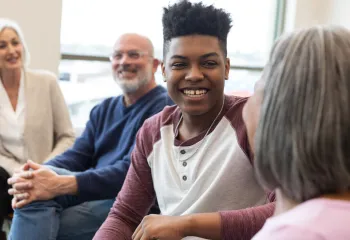A group of seniors speaking with a teen boy while sitting together in a circle.