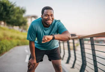 A man takes a break from jogging outdoors to check his smartwatch.