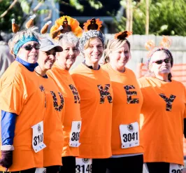 A group of women standing together. They are each wearing orange shirts with a letter on them. The shirts spell out "tirkey."