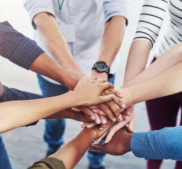 A diverse group of people standing in a circle. Their hands are stacked in the center.
