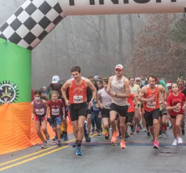 The Reindeer Romp starting line. A crowd of people wearing running gear are running toward the camera as the race starts.