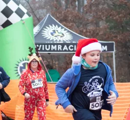 A boy wearing a Reindeer Romp shirt and a Santa hat runs during the annual Reindeer Romp race.