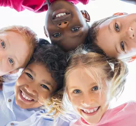 A diverse group of children laughing and playing. They are standing in a circle together and looking down at the camera.