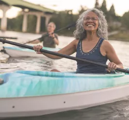 A senior woman kayaking smiles at the camera.