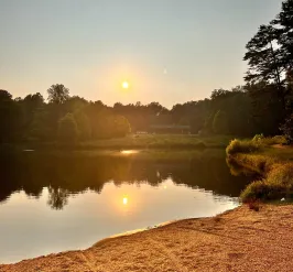 A view overlooking YMCA Camp Weaver's lake. There is a sunset in the background. The sun is warm and yellow and reflected in the lake. In the foreground is a path.