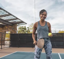 A woman holding a pickleball paddle stands outside on a court.