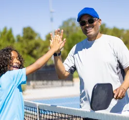 A father and young child playing pickleball together.