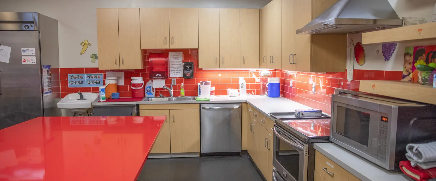 A photo of the kitchen at the Hayes-Taylor YMCA. There is red tiling beneath tan cupboards and a large tan kitchen island.