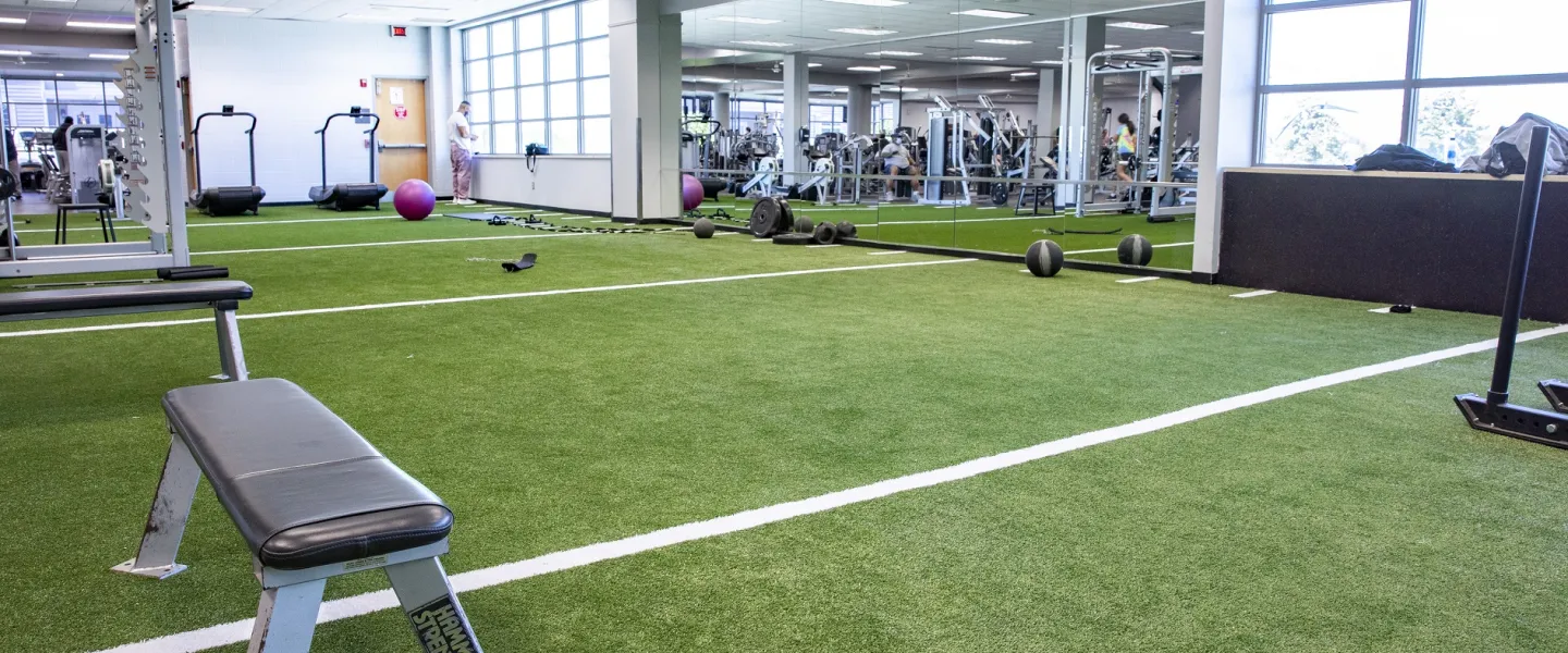 The turf fitness area at the Bryan YMCA. The floor is artificial grass turf and there are several weight machines in the room.