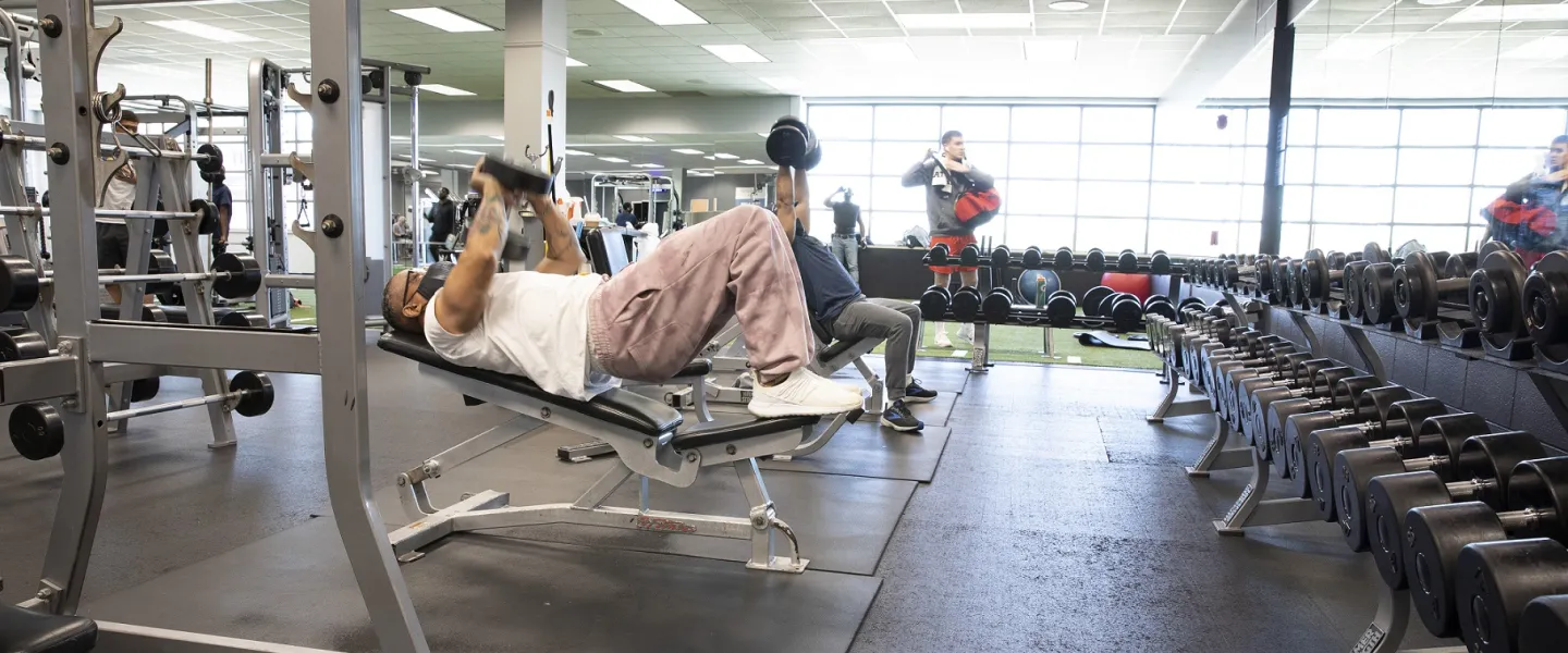 Two men lifting weights in the Bryan YMCA's weightlifting room. There is a man standing near the window at the rear of the room.