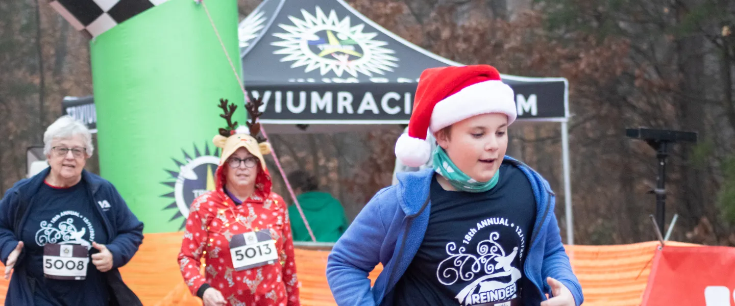 A boy wearing a Reindeer Romp shirt and a Santa hat runs during the annual Reindeer Romp race.