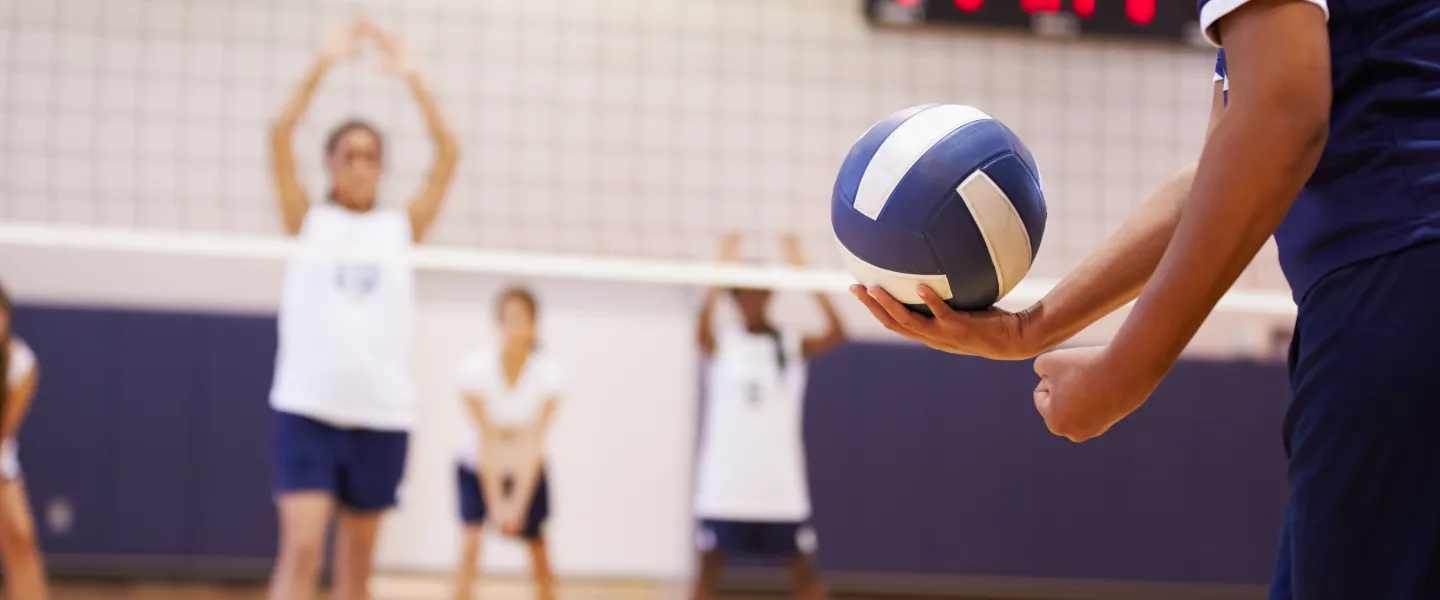 A group of girls playing volleyball. The camera is focused on a player preparing to serve a volleyball.