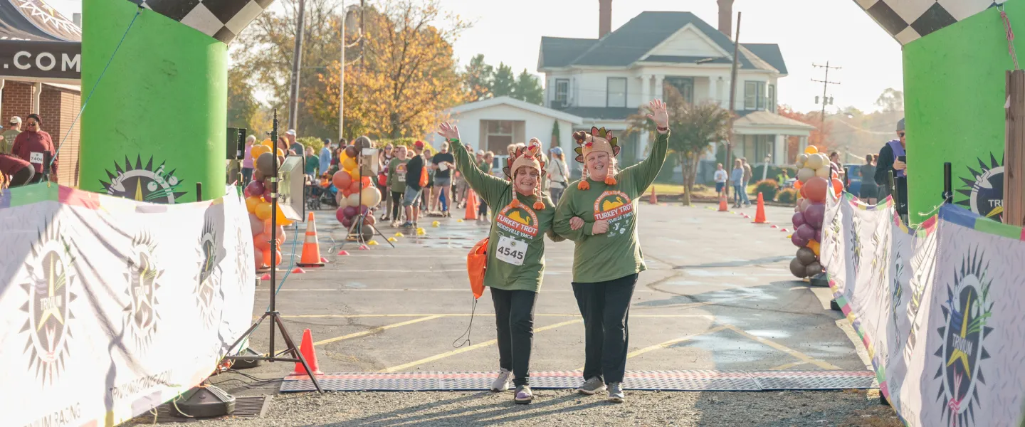 Two Turkey Trot runners arms interlocked, celebrating together as they cross the finish line.
