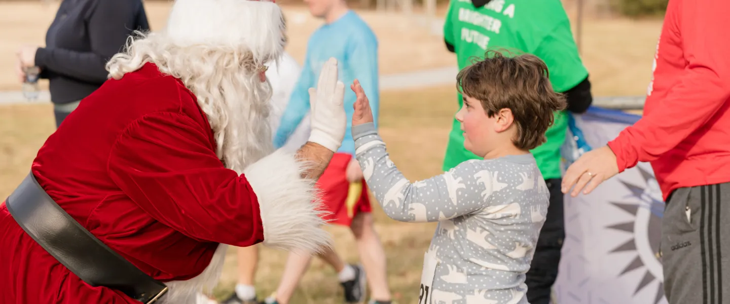 A man dressed as Santa at the Ragsdale YMCA Reindeer Romp giving a road race participant a high five.