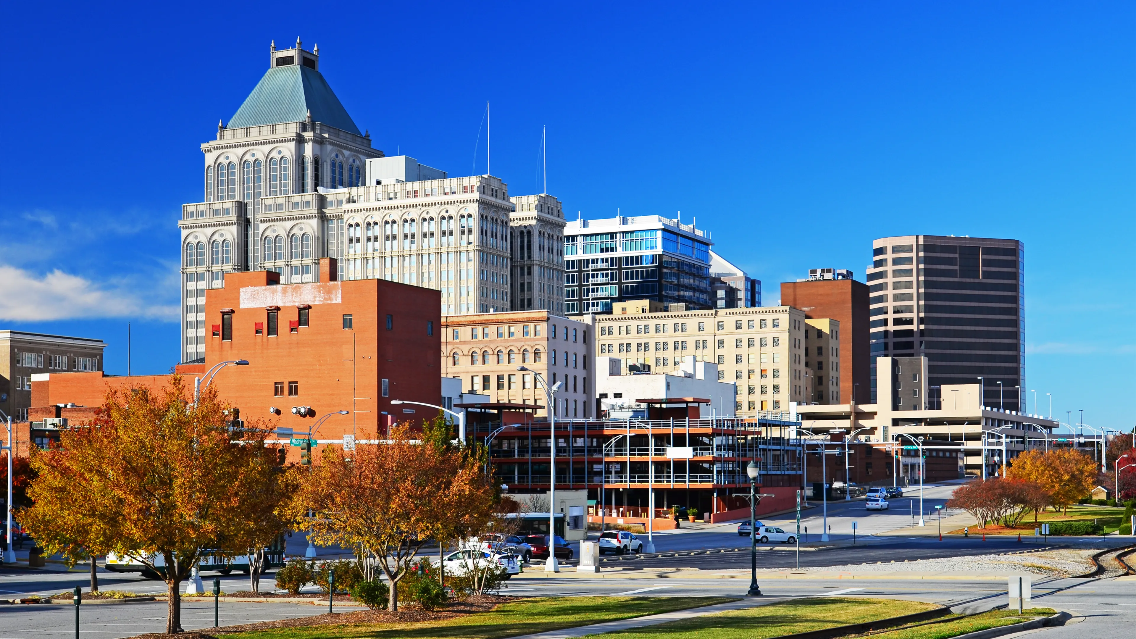 Greensboro, North Carolina during autumn. There are trees with orange leaves and the city skyline.