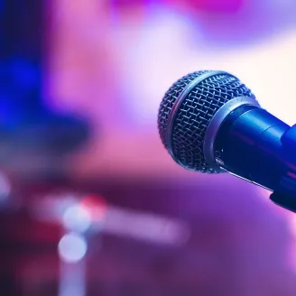 A close-up image of a microphone. There is a purple and blue background behind it.