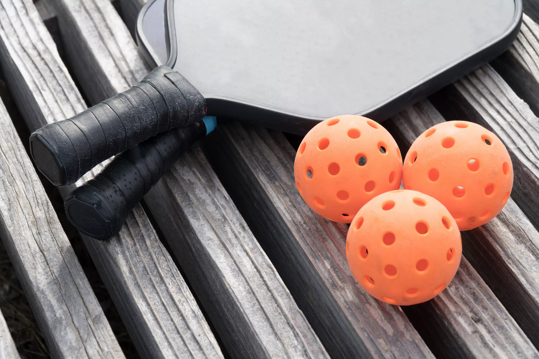 Two pickleball paddles and three balls sitting on a wooden surface.