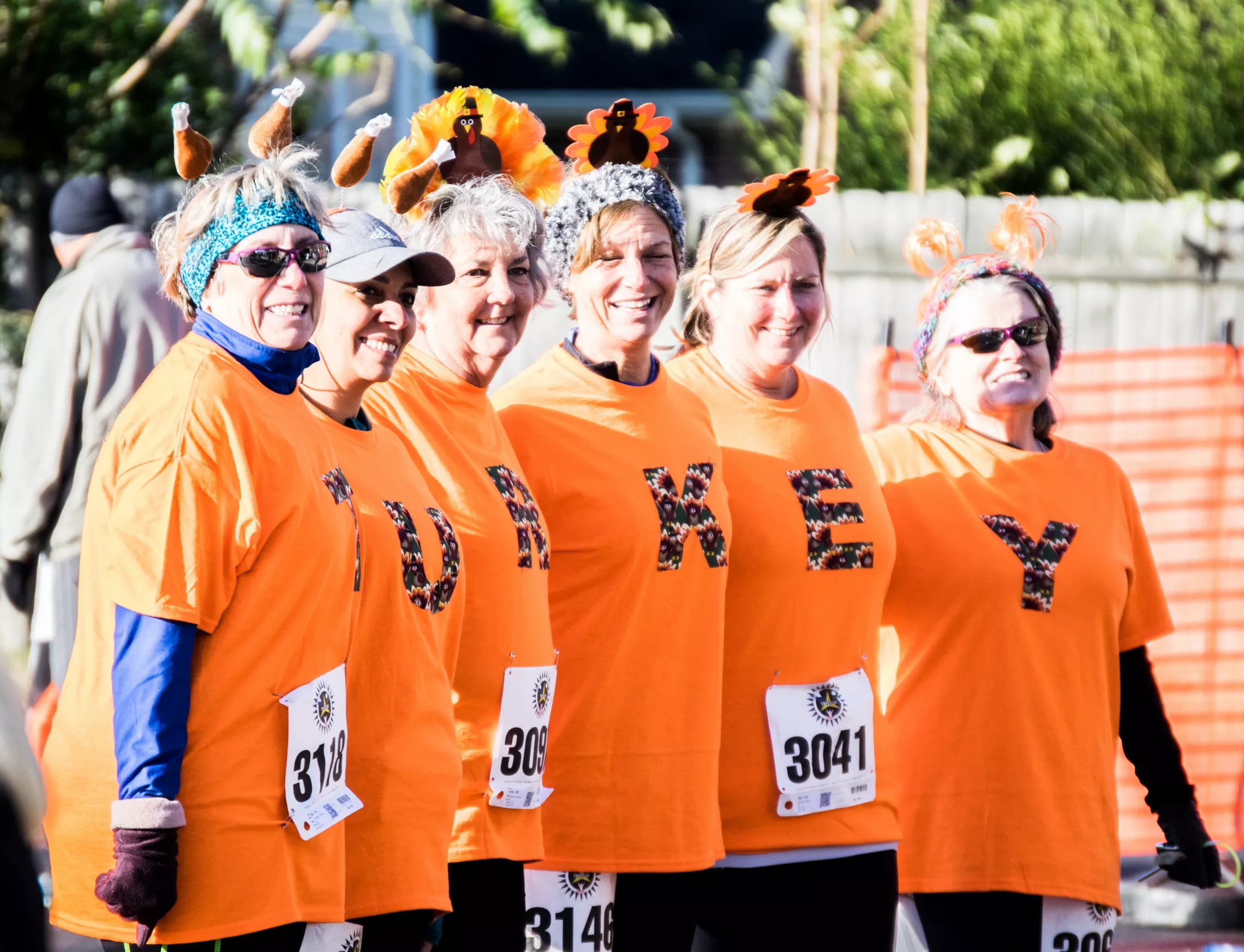 A group of women standing together. They are each wearing orange shirts with a letter on them. The shirts spell out "tirkey."