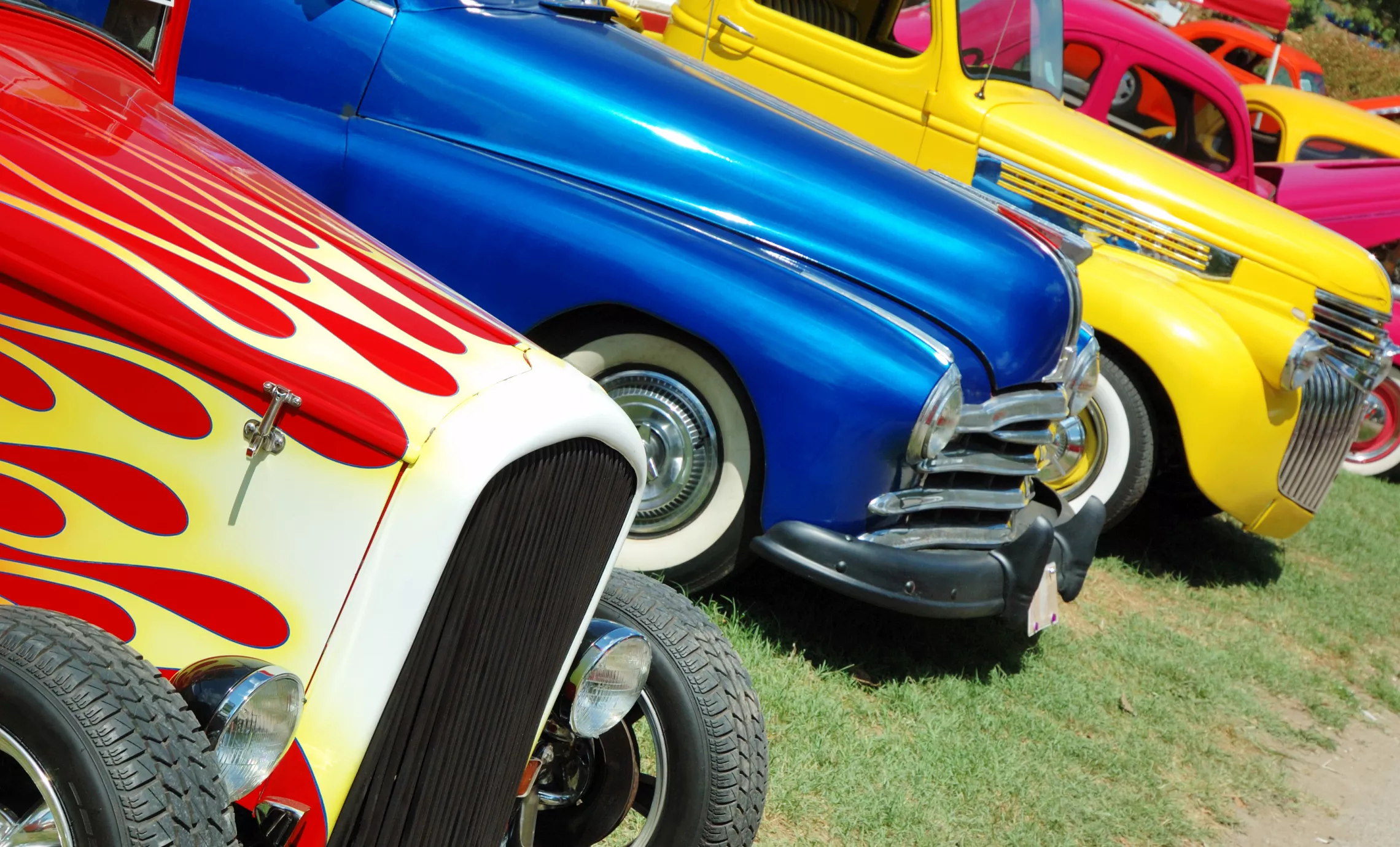 Colorful vintage cars are lined up in the grass.