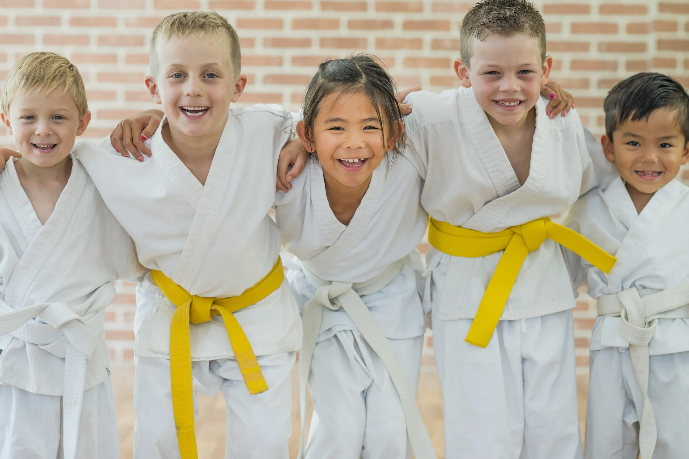 A diverse group of children smiling at the camera. They are dressed for a tae kwon do class.