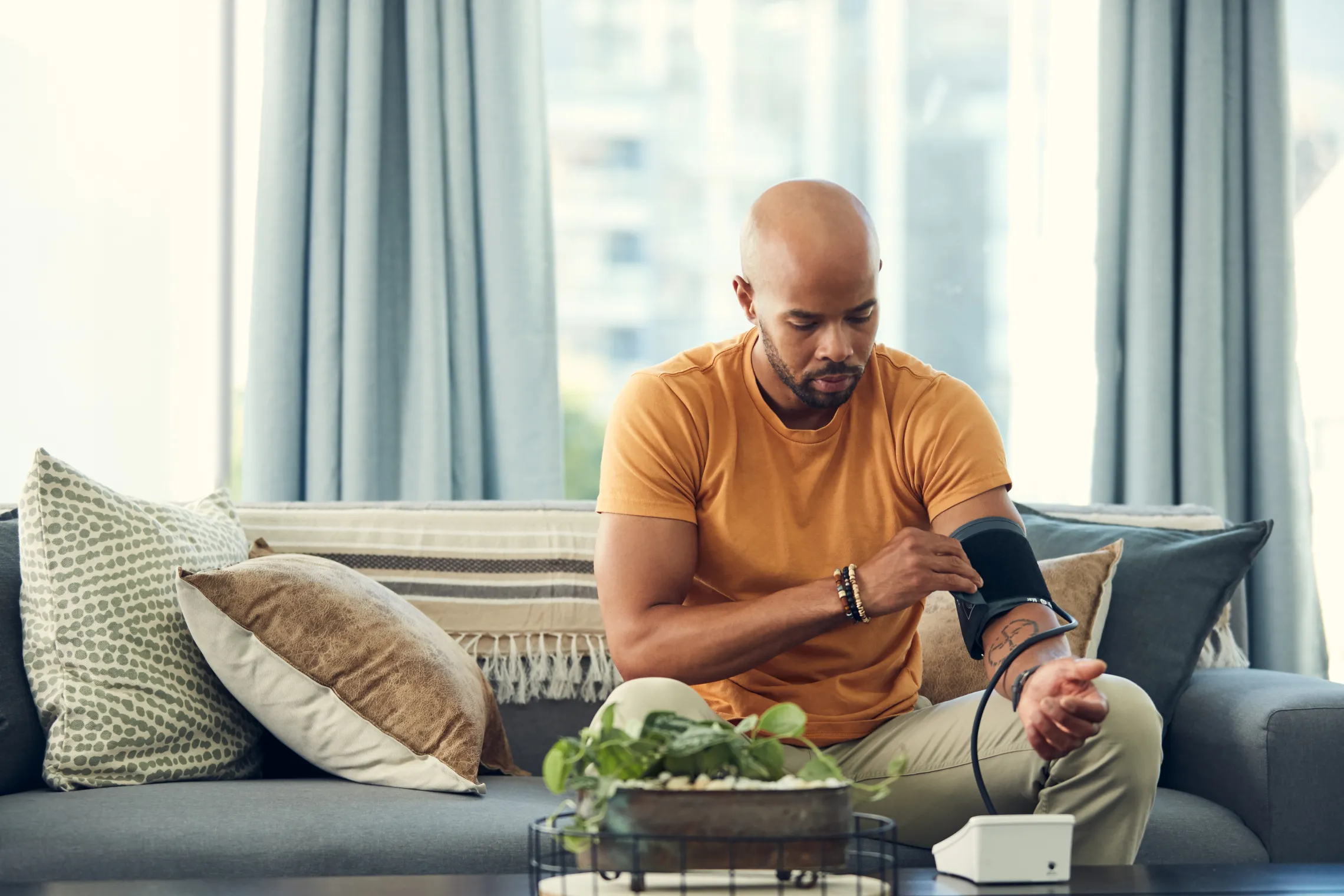A man monitoring his blood pressure in his home using a blood pressure cuff. He is sitting on a couch.