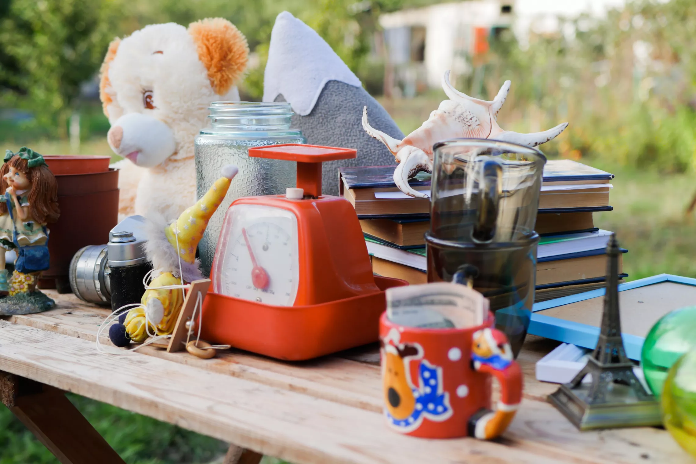 A photo of a collection of items on a wooden table. Some of the items include a mug, a stuffed bear, and a stack of books.