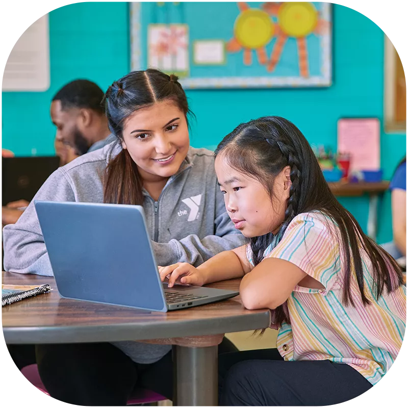 A Y team member helping a young girl work on a laptop.