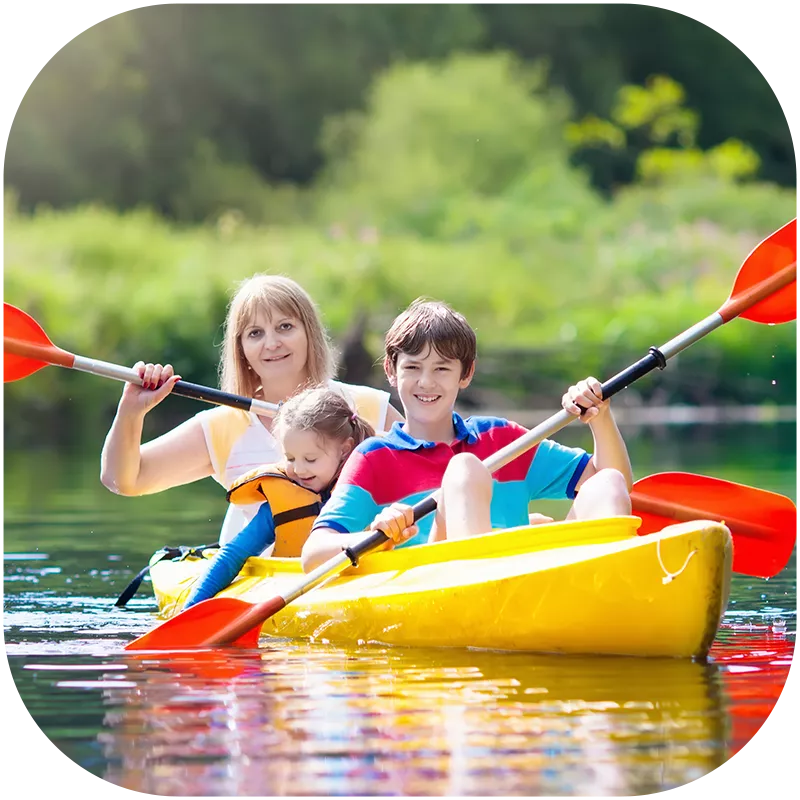 A mother and her two children, a young girl and a boy, kayaking together on a lake. They are smiling at the camera.