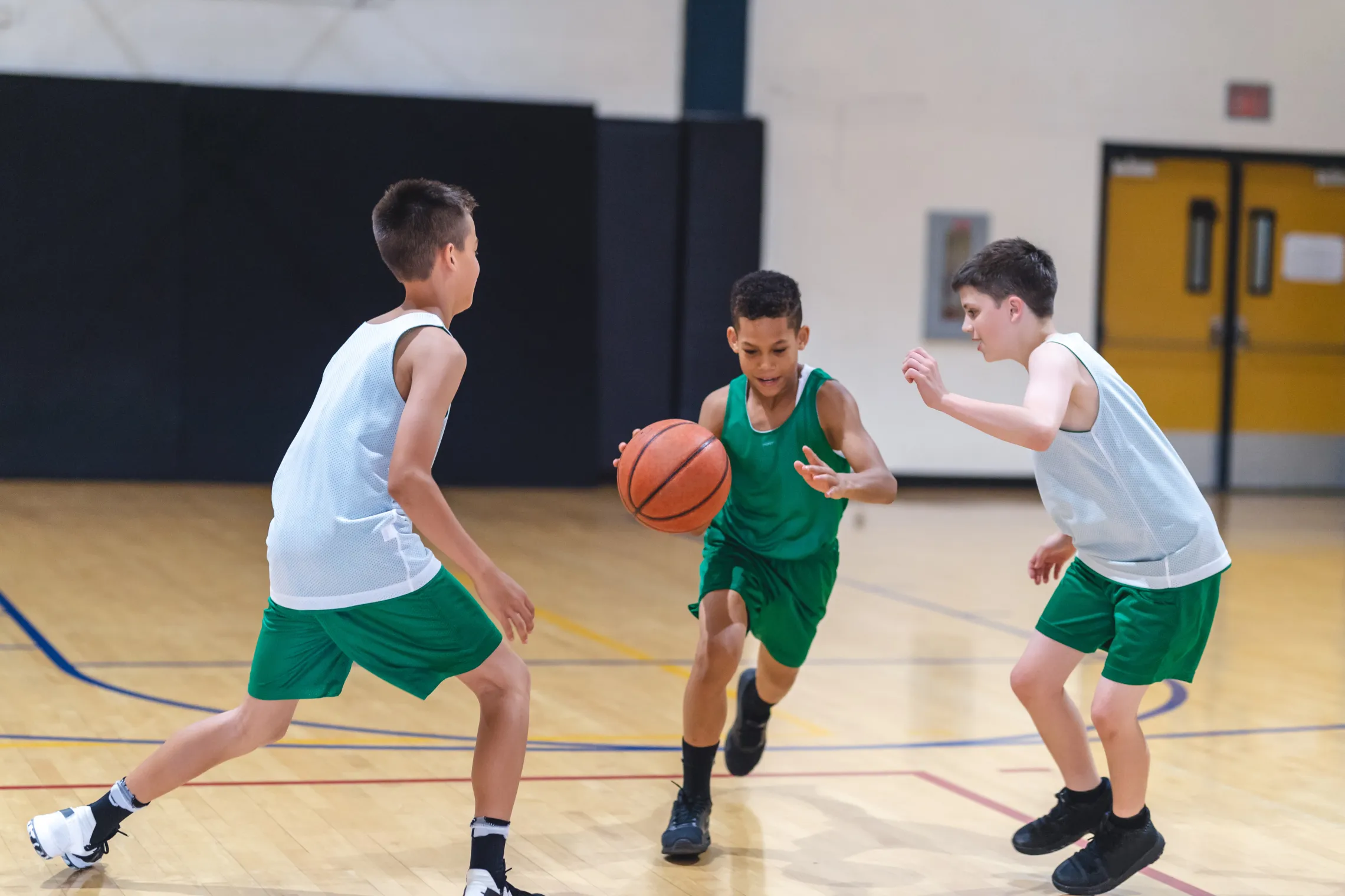 Three young boys playing basketball in a gym.