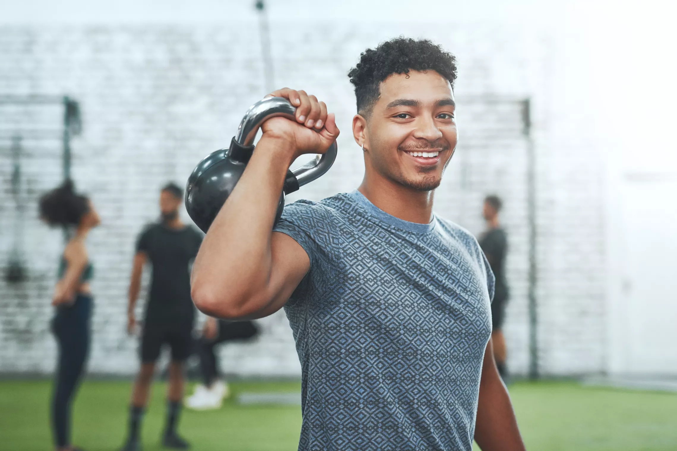 A man lifts a kettlebell over his shoulder while smiling at the camera.