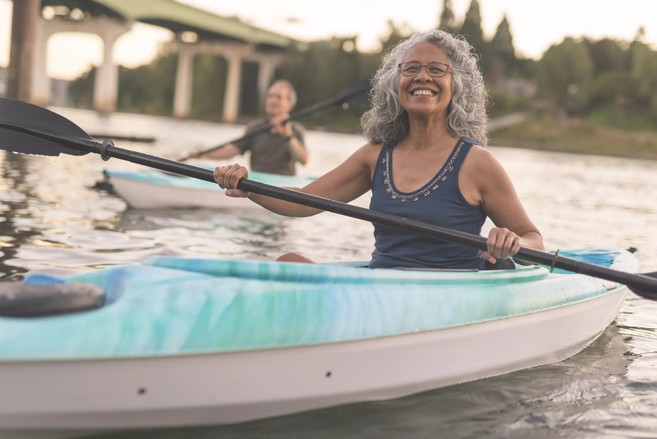 A senior woman kayaking smiles at the camera.