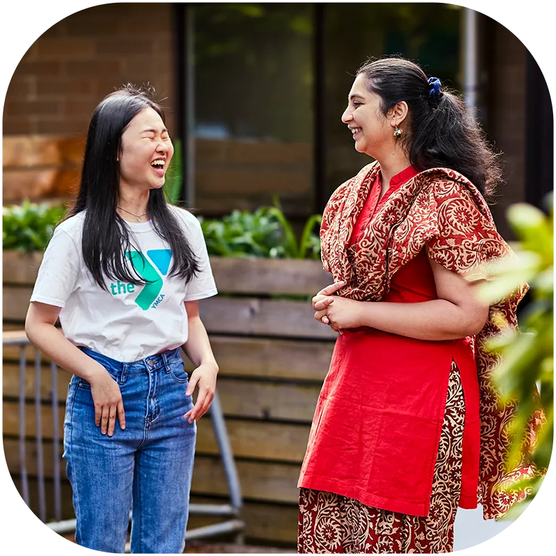 Two woman standing outdoors on a sunny day laugh together.