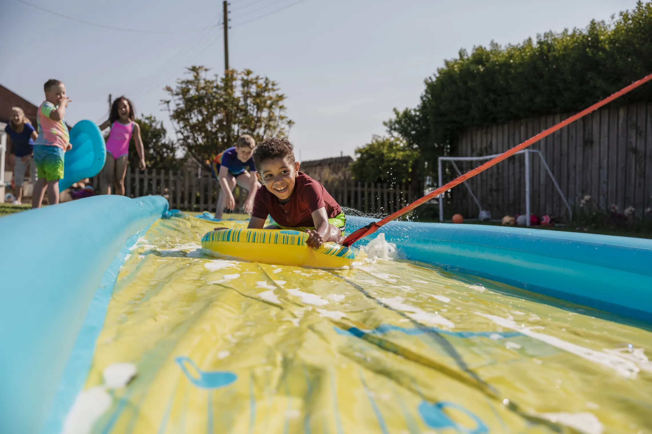 A group of children having fun outside on a slip and slide.