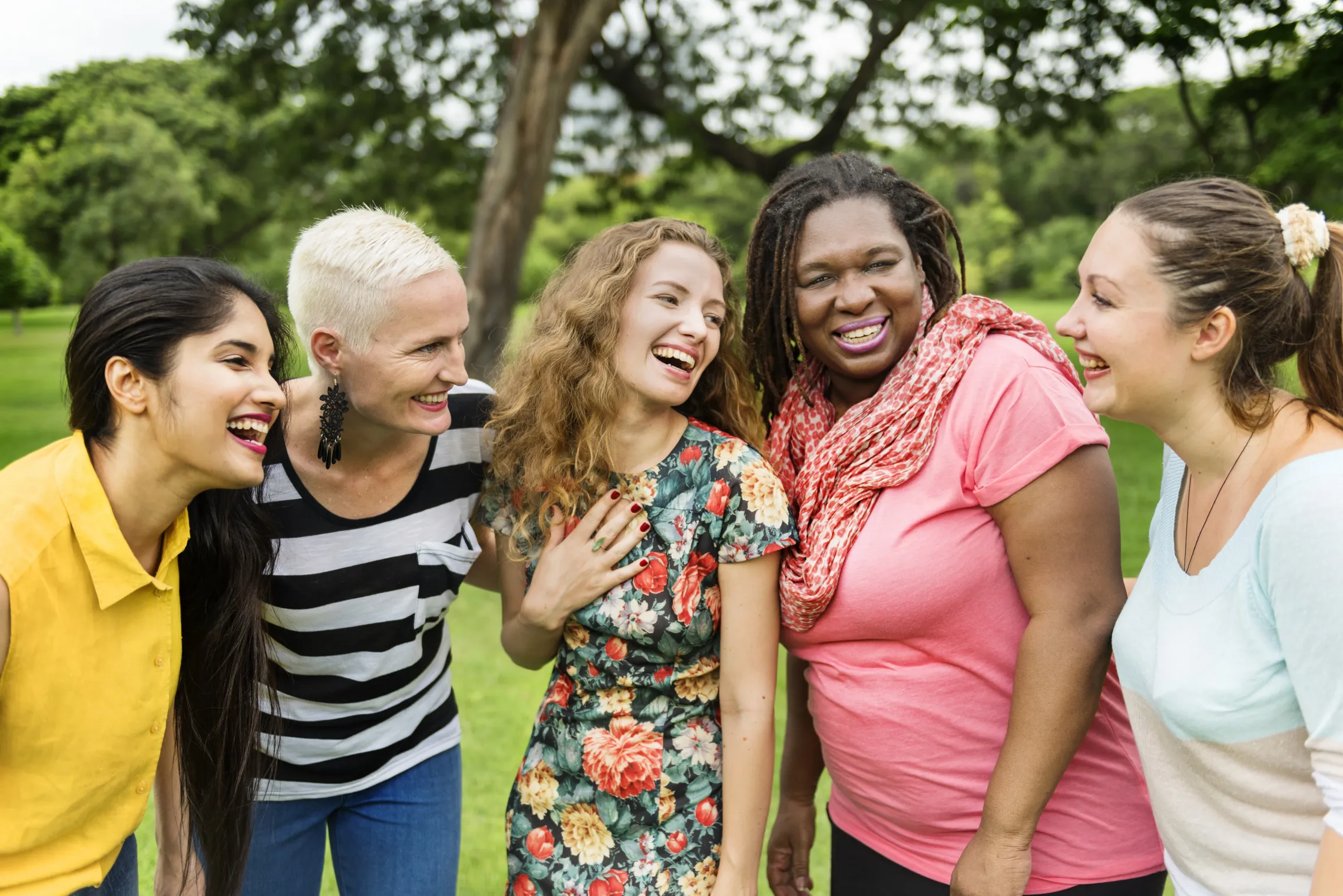 A group of diverse women standing outside together and laughing.