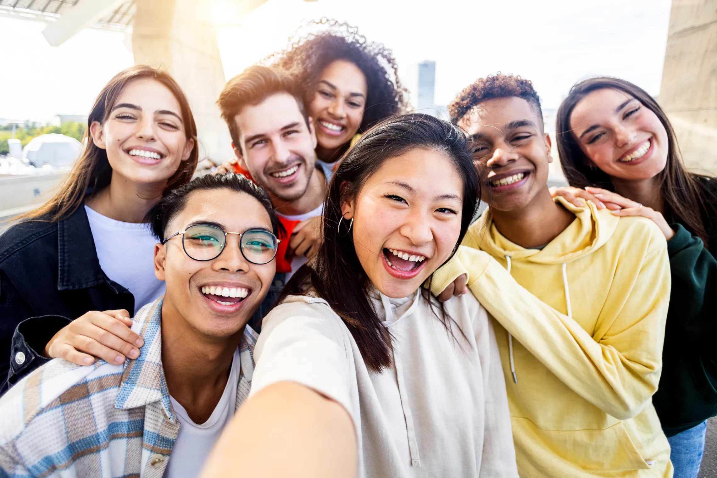 A diverse group of teens laughing together. They are smiling into the camera and taking a selfie.