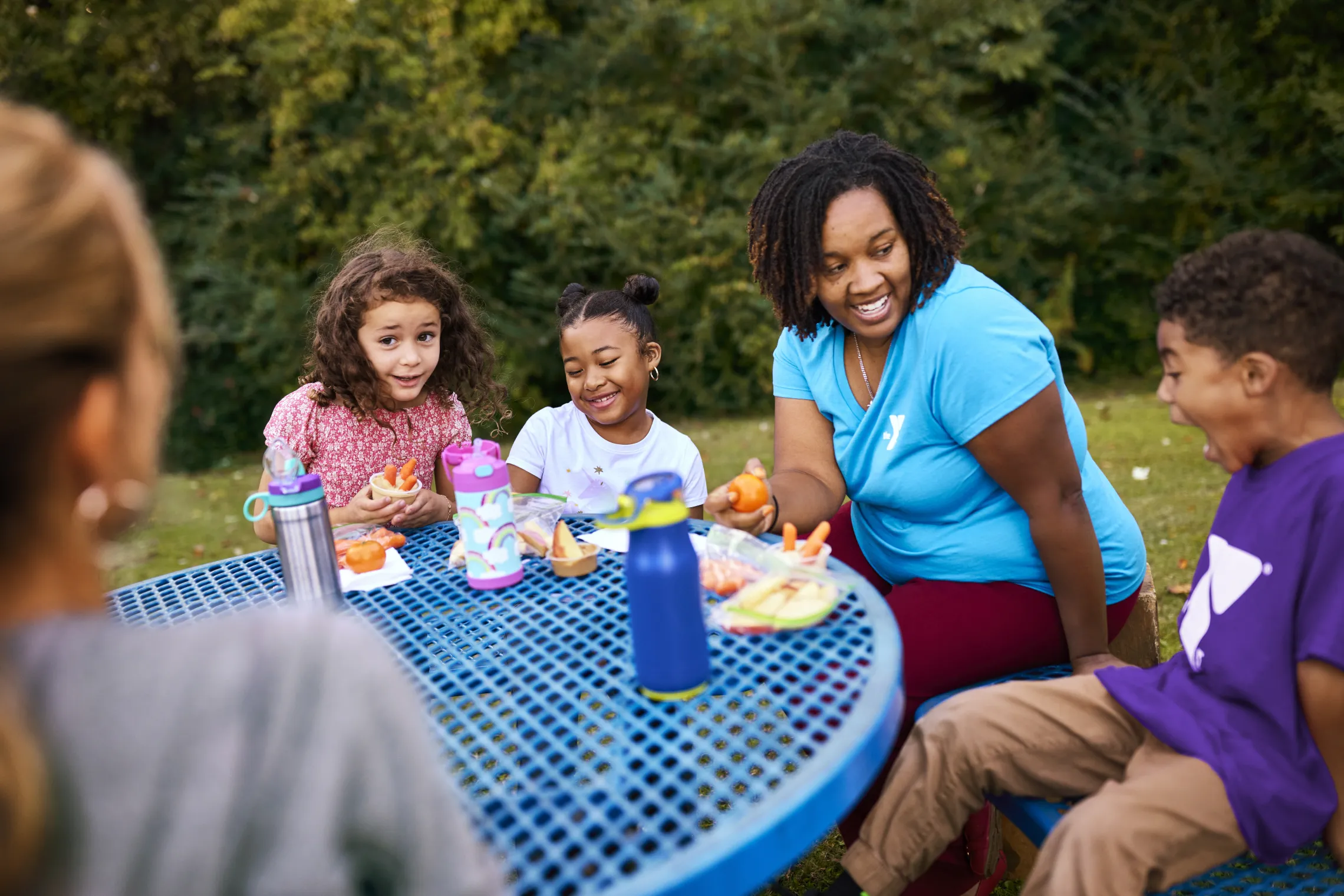 A group of children eating lunch outside during Y Summer Camp. A Y team member is sitting with them.