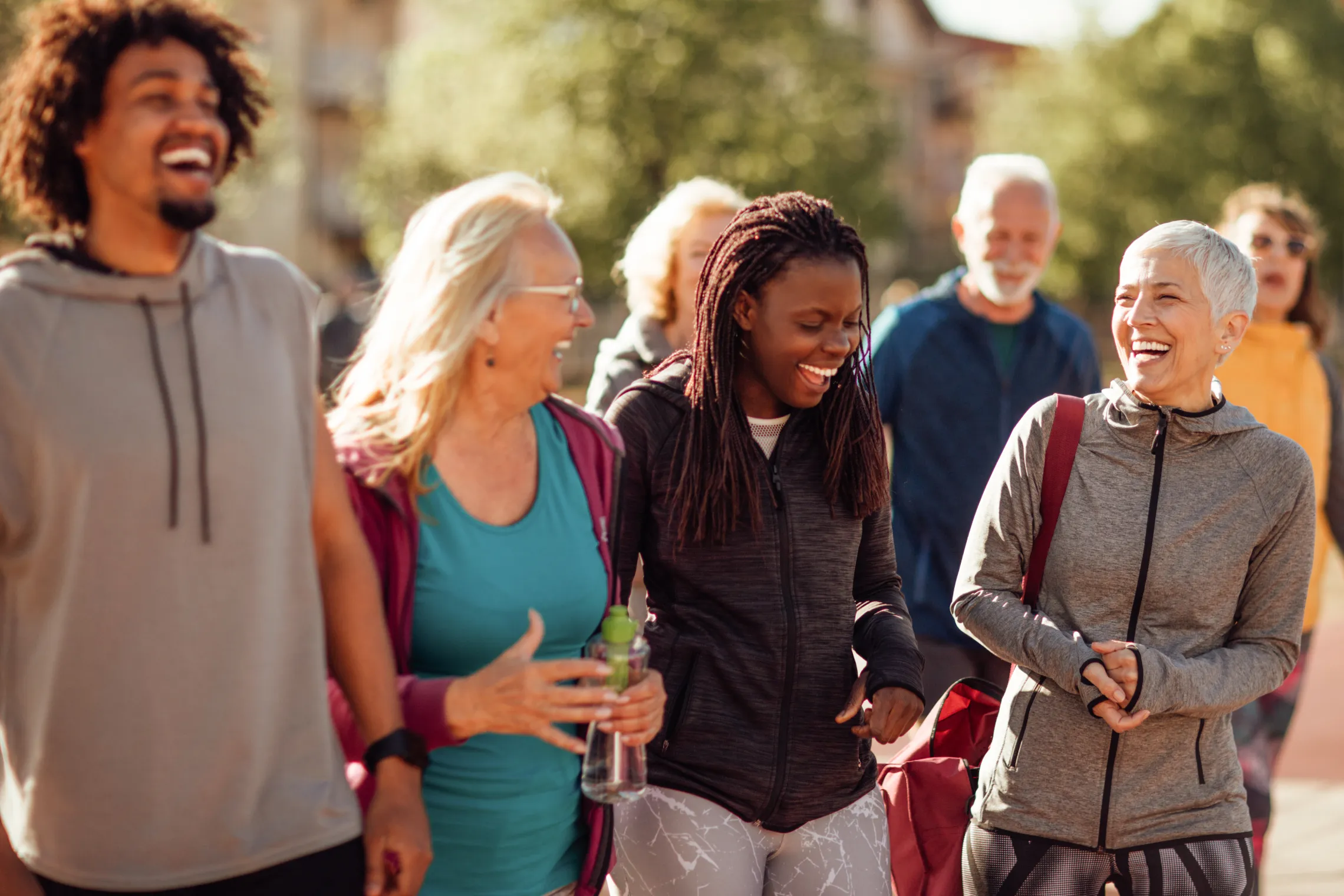 A diverse group of people outdoors wearing exercise clothing. They are laughing together.