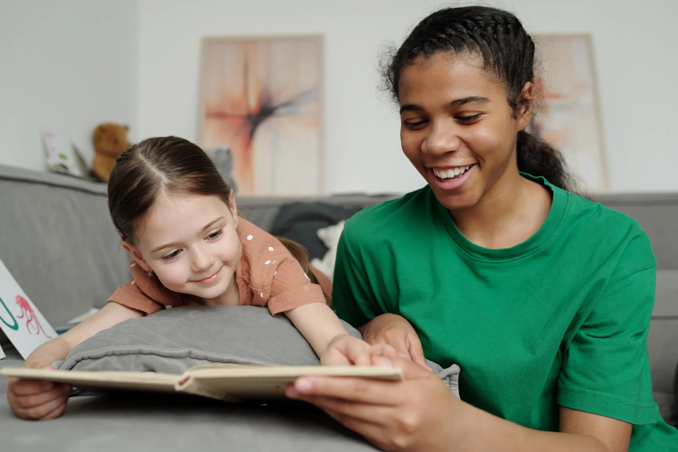 A teenage girl reads to a young girl. They are both smiling.