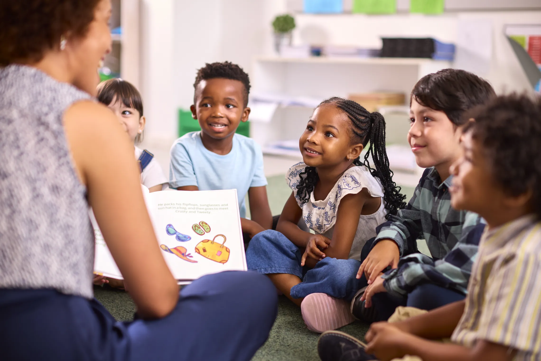 A diverse group of young children sitting in a circle as they listen to a teacher read a book.