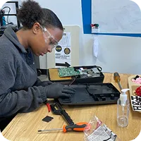 A teen works on an electrical project. She is wearing safety glasses and gloves.
