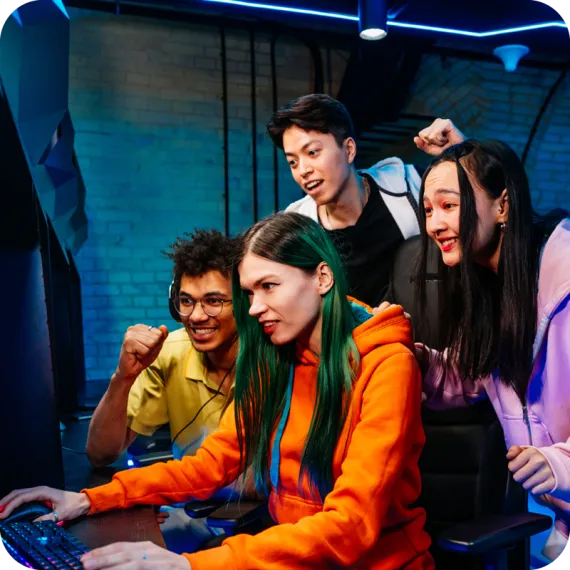 A diverse group of teens watches an eSports teammate playing a game on a desktop computer.