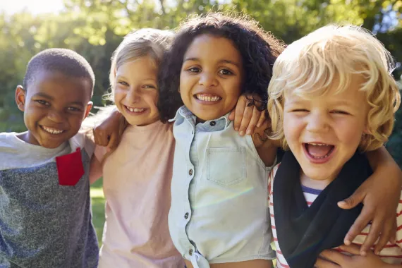 A diverse group of young children smiling together outdoors.