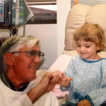 A little girl in the hospital smiles with her grandfather.