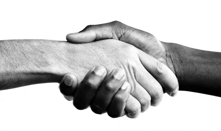 A black and white photo of a handshake from people of two different ethnicities. One of the hands is dark-skinned and the other hand is light-skinned.