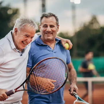 Two older adults laughing and bonding during tennis match.