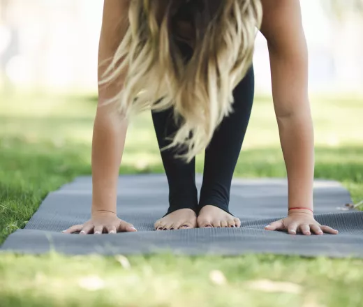 A woman stands on a mat while doing yoga outdoors.