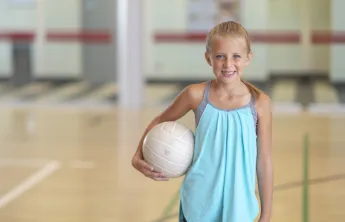 A little girl smiling at the camera while holding a volleyball.